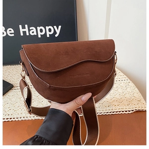Close-up of brown suede saddle bag with wide fabric strap and golden hardware