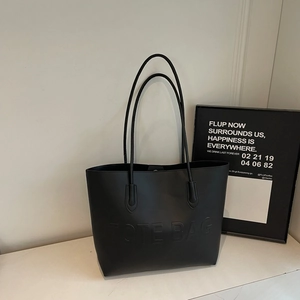 Grande borsa tote nera minimalista con scritte in rilievo su piano di marmo