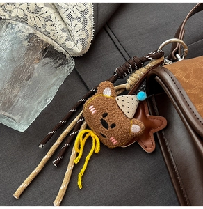 Detail of cute plush bear charm with tassels on a brown leather shoulder bag handle