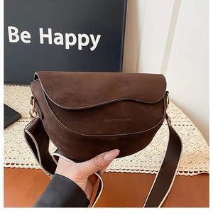 Close-up of deep brown suede saddle bag with wave-shaped flap and wide fabric strap