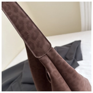 Detail of wide shoulder strap stitching on a brown suede tote bag with diamond texture