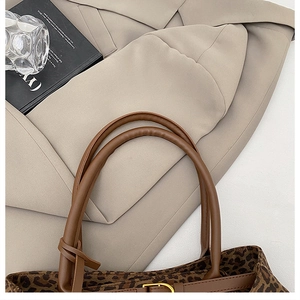 Macro view of leopard print tote bag with brown leather handles and golden metal buckle