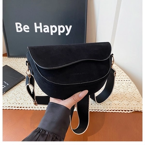 Detail of black suede saddle bag featuring wide bicolour strap and gold metal hardware