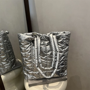 Silver quilted tote bag with metallic finish on a white display stand in a minimalist setting