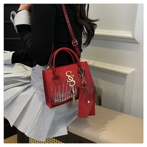 Detalle del bolso rojo grabado de cocodrilo con logo SSS dorado y borla elegante