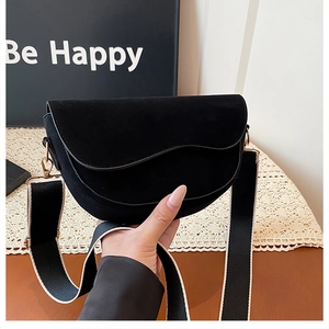 Detail of black suede saddle bag with wavy flap and black-white woven wide strap