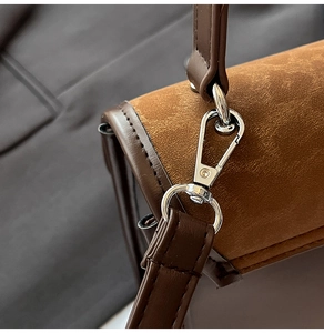 Close-up of brown suede bag with smooth leather trim and polished silver metal buckle