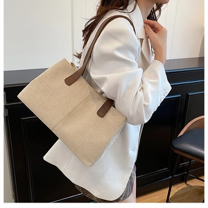 Dettaglio della borsa tote beige con manici in pelle marrone indossata su blazer bianco
