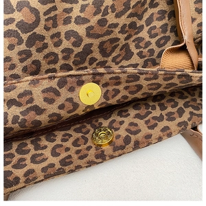 Close-up of golden magnetic snap closure on leopard print tote bag with brown leather strap