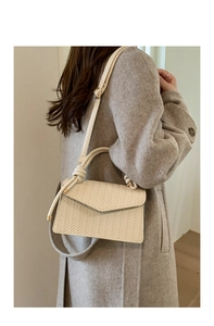 Detailed macro view of cream woven texture and V-shaped flap on a stylish crossbody bag