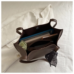Detail view of large brown pleated tote bag interior holding a tablet and umbrella
