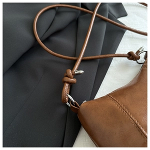 Detail of retro brown leather bag showing long thin strap with knot and silver ring connector