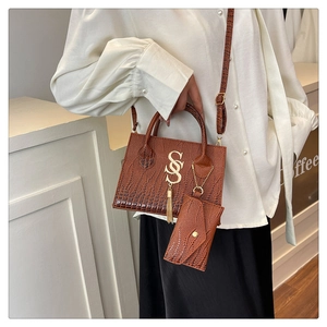 Detalle de bolso marrón con textura de cocodrilo, logo SSS dorado y borla de flecos