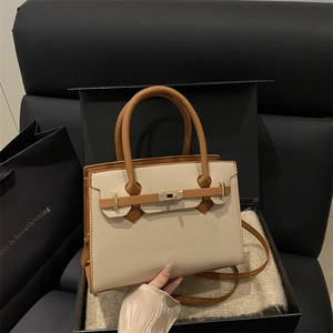 Borsa in pelle beige e caramello con fibbia in metallo su divano in pelle nera