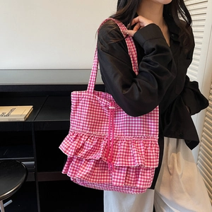 Pink and white gingham tote bag with ruffled edges and drawstring on shoulder model