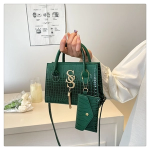 Detalle de bolso verde bosque con patrón de cocodrilo, logo SSS dorado y estuche