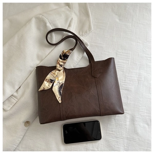 Detail of vintage brown leather tote bag with printed silk scarf and smooth texture