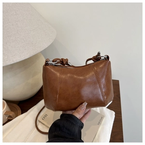 Close-up of a brown leather half-moon bag featuring a knotted strap and silver zipper detail