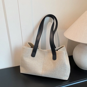 Borsa tote minimalista in tela beige con manici neri in pelle posata su tavolo