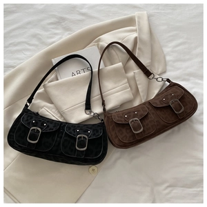 Detail of retro underarm bags with dual buckled pockets on white fabric and book