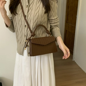 Brown woven texture crossbody bag shown on model with beige sweater and white skirt