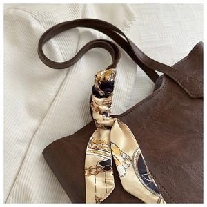 Detail of dark brown faux leather tote with floral silk scarf on white textured fabric