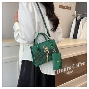 Detalle del bolso de mano verde oscuro con textura de cocodrilo, logo SS dorado y borla