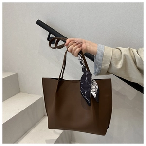 Close-up of warm brown faux leather tote bag with stylish black and white silk scarf handle