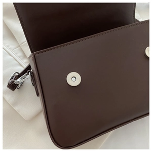 Detail of dark brown crossbody bag with dual silver magnetic buckles and matte finish