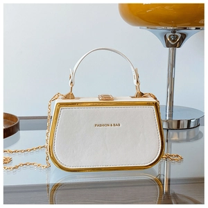 Close-up of white leather box bag with gold metal frame and decorative chain strap