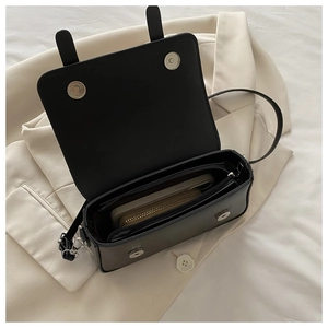 Detail of the black rectangular crossbody bag showing magnetic buckles and interior storage