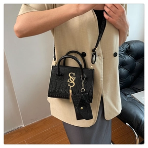 Detalle de bolso negro textura cocodrilo con logo S dorado y colgante de borlas