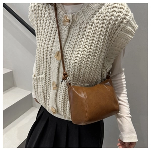 Close-up of brown synthetic leather crossbody bag with decorative stitching and knot detail