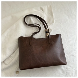 Detailed view of brown leather tote bag with silk scarf on white corduroy background