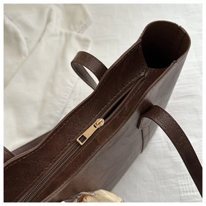 Detail of dark brown tote bag showing golden zipper closure and vintage leather texture
