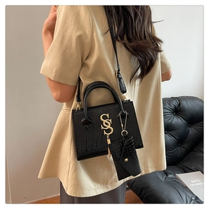 Detalle de bolso bandolera negro con relieve de cocodrilo, logo S dorado y minibolso