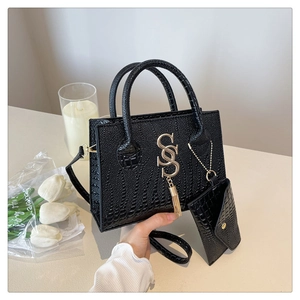 Detalle de bolso negro textura cocodrilo con logo SS dorado y mini bolso colgante