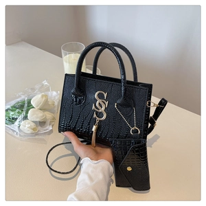 Detalle de bolso negro efecto cocodrilo con colgante de logo S dorado y flecos largos