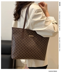 Detail of a brown tote bag with M letter monogram pattern and gold metal logo plaque