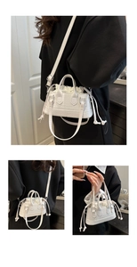 Detail of white crocodile pattern handbag featuring a drawstring closure and silver hardware