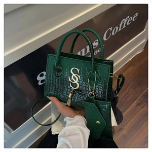 Detalle de bolso verde oscuro grabado de cocodrilo con logo dorado y monedero pequeño