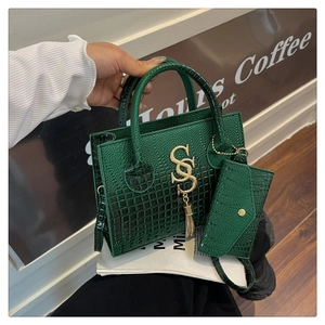 Detalle de bolso de mano verde esmeralda con diseño de cocodrilo, colgante dorado y estuche
