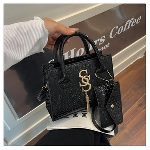 Detalle de bolso negro con textura de cocodrilo, logo dorado de doble S y borla lateral