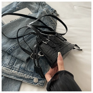Detail of black crocodile pattern leather handbag with strap on denim jacket background
