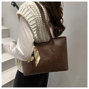 Detail of vintage brown tote bag with silk scarf on textured leather shoulder strap
