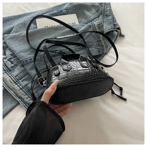Detail of black crocodile texture handbag placed on a denim jacket with metal clasp