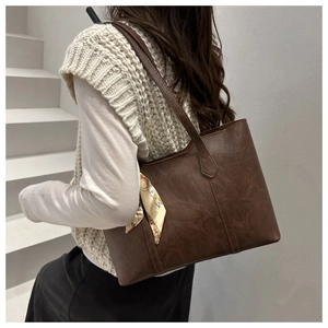 Detail of a brown leather tote bag with lychee texture and a decorative floral silk scarf