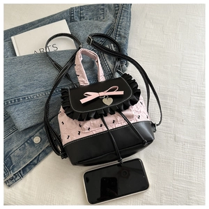 Détail du sac à dos rose et noir avec nœud et breloque en cœur sur un fond de tissu blanc
