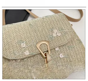 Close-up of floral embroidery and gold triangular metal clasp on beige straw saddle bag