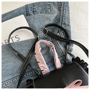 Détail du sac à main en cuir noir avec anse à nœud rose et bandoulière réglable